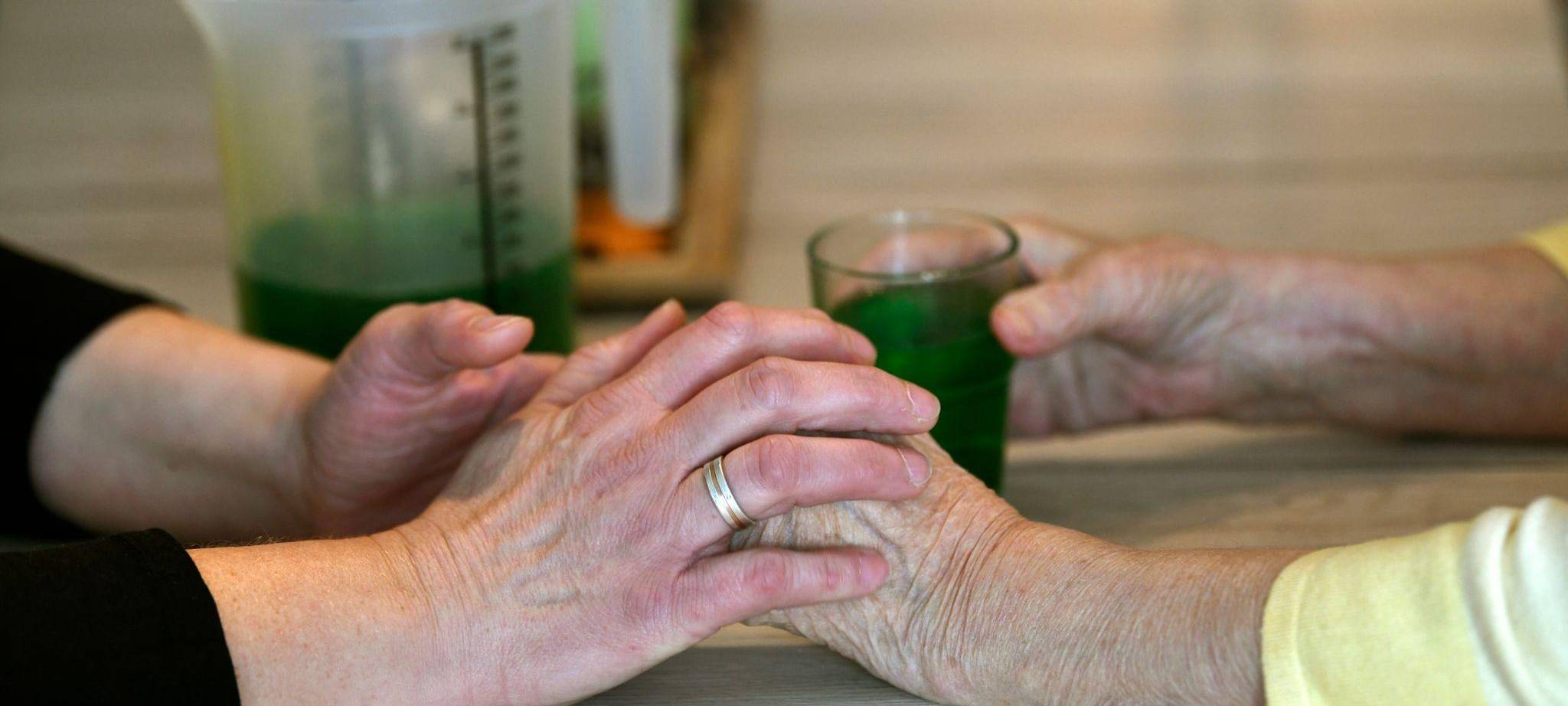 Frau fasst die Hände einer demenzkranken Frau in Demenz-WG an